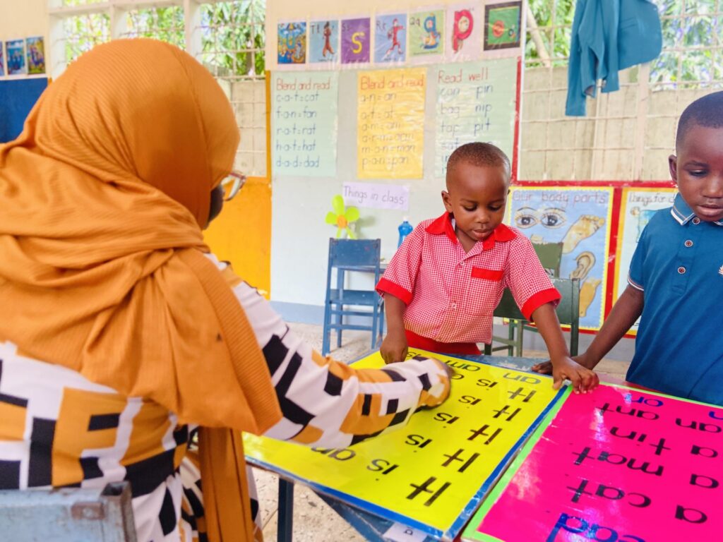 A mother follows along as learners read from the phonics boards.