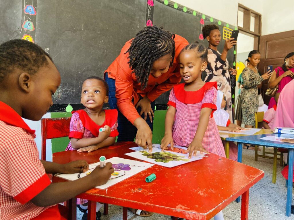 A teacher guides learners through their colouring work as parents look on.
