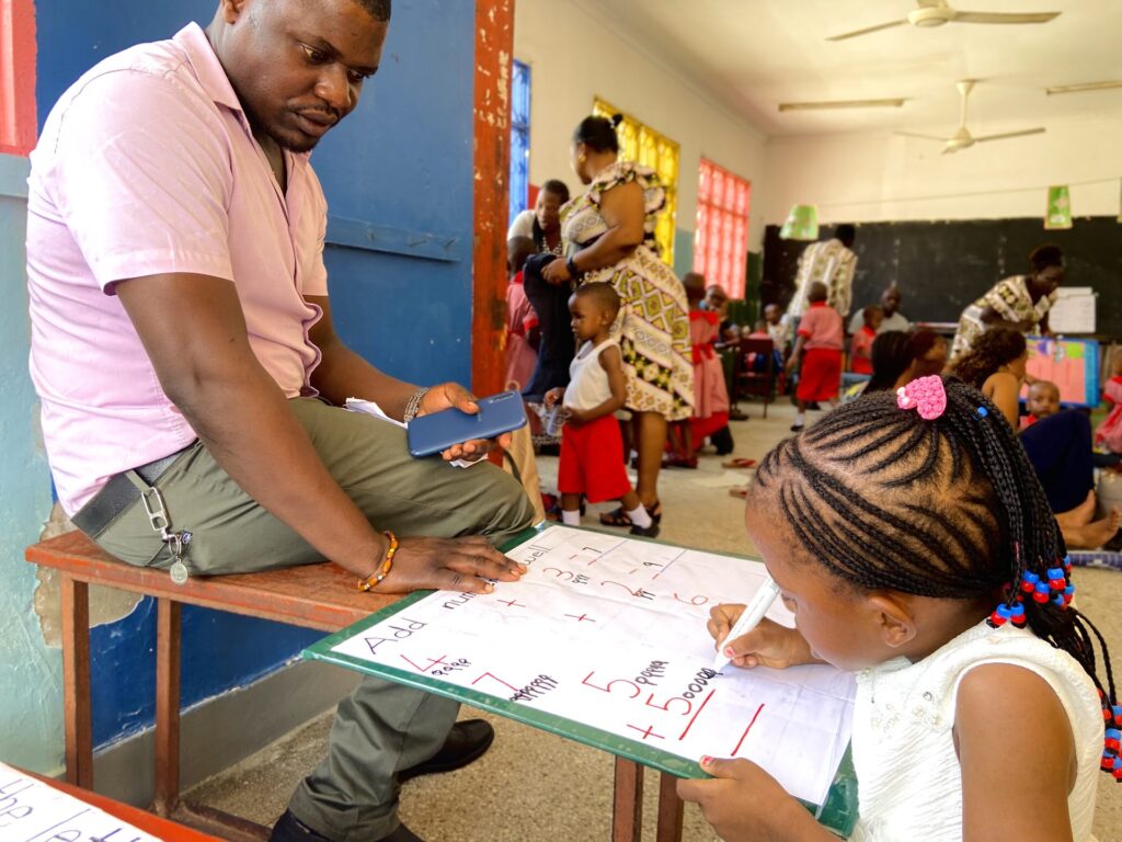 A father watches his daughter work through addition sums.
