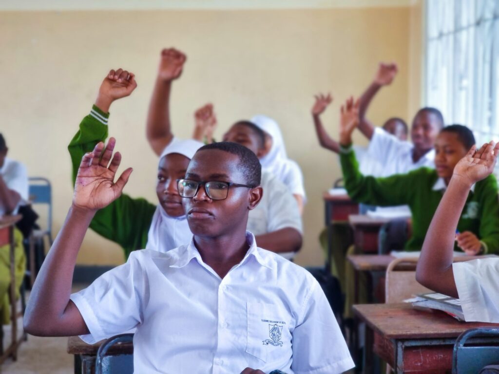 Hands shoot up in a Tusiime Secondary classroom.